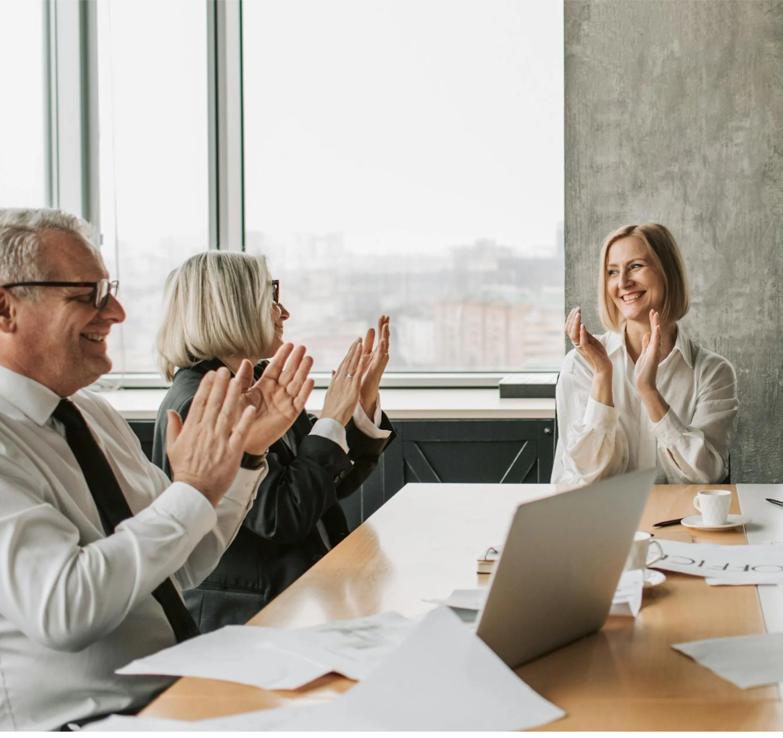 Business professionals clapping in meeting room with laptop and coffee
